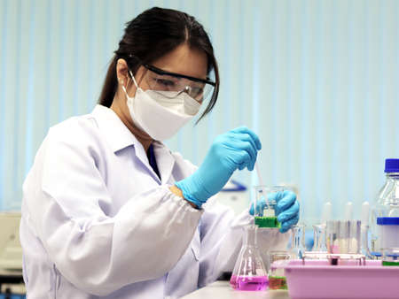 The scientist wears PPE do the chemical experiment in laboratory, with pale pink solvent solution from pouring reaction indicator acid titration experiment, analysis compounding in wastewater sample.の写真素材