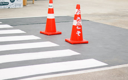 Orange traffic cones standing in a row beside a crosswalk. Traffic symbol sign on grey road with white stripe for warning to walk across the road with carefully and safety. Backgroの写真素材