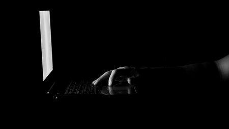Low key male hand touching on laptop mouse pad with the dark background. Concept for scammers awareness.の写真素材