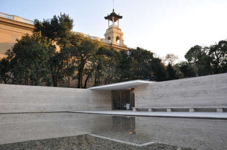German Pavilion in Barcelona with large reflecting pool and trees lined up around marble wallsのeditorial素材