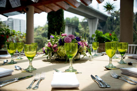 Stylish table setting for an open-air wedding with green wineglasses, silverware and linen on a table on a sunny urban patioの写真素材