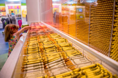 Cute little girl selecting art supplies in a store reaching up to choose colorful wax crayons from the displayのeditorial素材