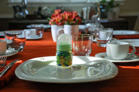 White china with silver and gold inlaid detail, red table cloth and flowers. Baby bottle filled with...