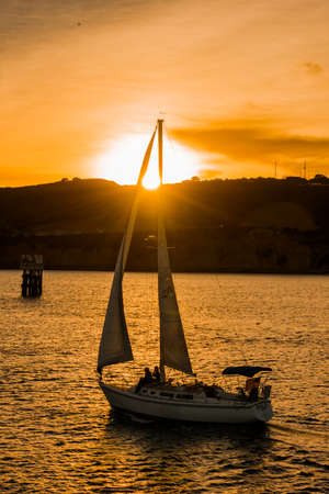 Tranquil scene with sailboat sailing in ocean against amber sky at sunsetの写真素材