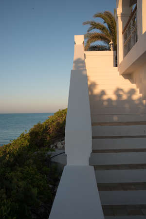 Flight of exterior steps on a luxury tropical villa in the Caribbean overlooking the ocean at sunset with a glow in the sky on the horizon and fronds of a palm treeの写真素材