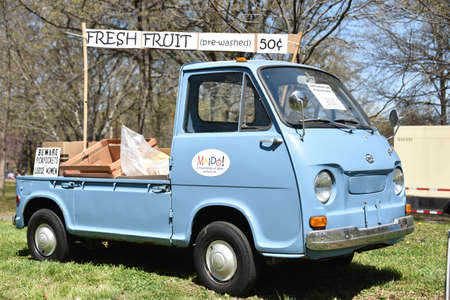 Restored blue 1960s Subaru truck used to sell fresh fruit parked on green grass with advertising...