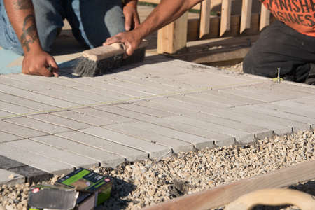 Close up view of two workers laying brick on sand layer on sunny dayの写真素材