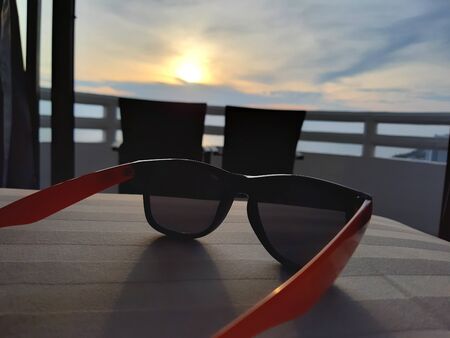In the summer vacation. Sunglasses lay down on the hotel bed. facing to the scenic view of sunset at the balcony.の写真素材