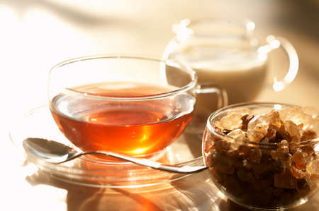 A cup of tea, brown sugar in a glass sugar bowl and a small milk jugの写真素材