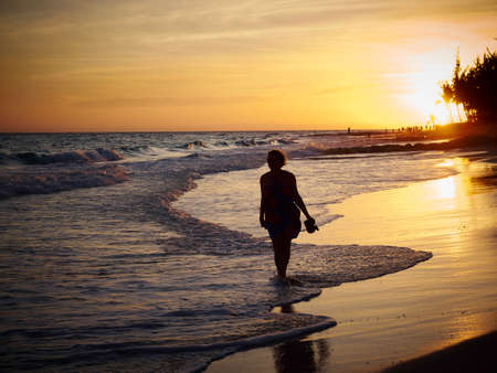 Woman Walking Along Tropical Beach At Sunset in Barbadosの写真素材