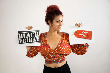 Girl with mischievous face holding two Black Friday and Low Price signs with her hands. Young woman...