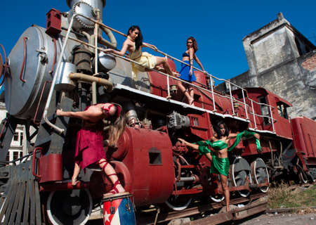 Four girls dressed in different colors posing on an old train with a drum in an ancient cityの写真素材
