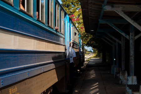 Blue carriages of an old train on the lines in a country town, parked on an old platform, a man...