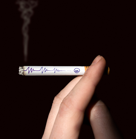 Symbolic drawing on a burning cigarette in a man's hand, isolated on a black backgroundの写真素材
