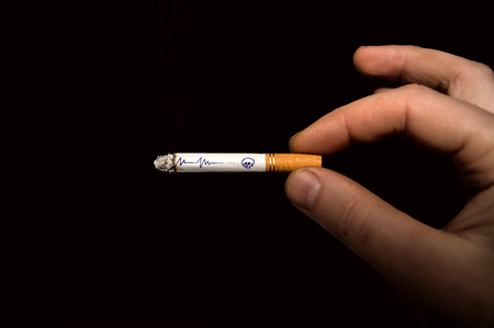 Symbolic drawing on a burning cigarette in a man's hand, isolated on a black backgroundの写真素材