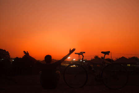 Silhouette freedom man sitting near bicycle on sunset.の写真素材