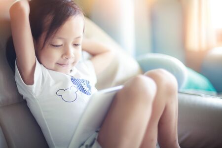 Cute child girl  relaxing while sitting  in front of a tablet at a home,Hi key style.