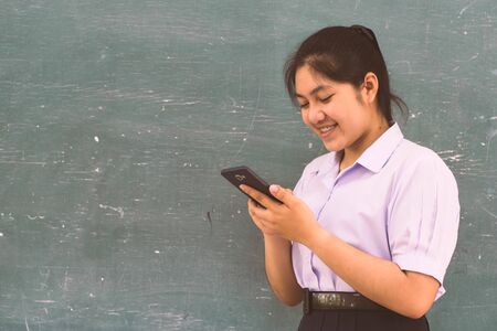 Beautiful girl student playing smartphone with smile in the classroom.