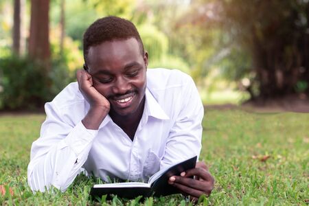 African man lying on the grass and reading a bookの写真素材