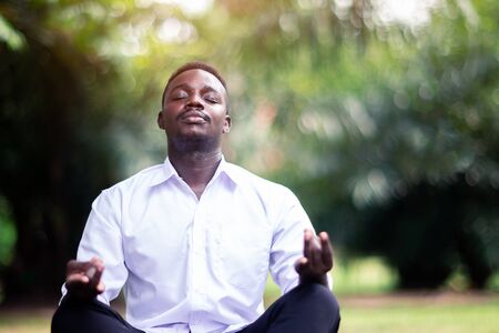 African business man is meditating on green grass in the parkの写真素材