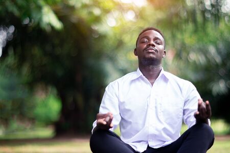 African business man is meditating on green grass in the parkの写真素材
