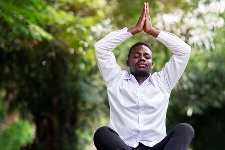 African business man is meditating on green grass in the park