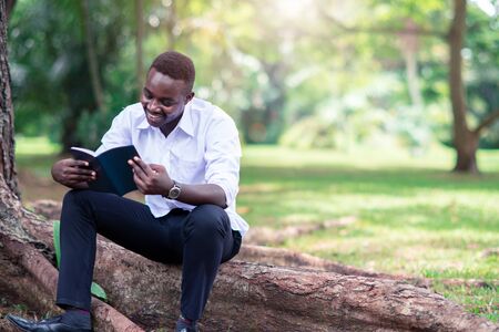 African man reading a book in the parkの写真素材