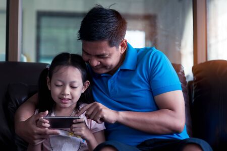 Asian Father and his daughter using smartphone at homeの写真素材