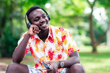 African man listening to music from smartphone with earphones against green natural background.の写真素材