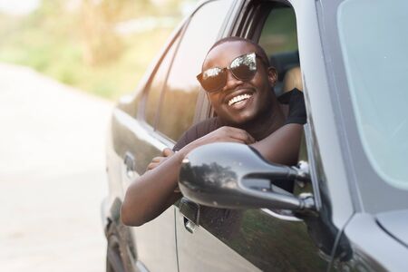 African man driver Wearing sunglasses and smiling while sitting in a car with open front window.の写真素材