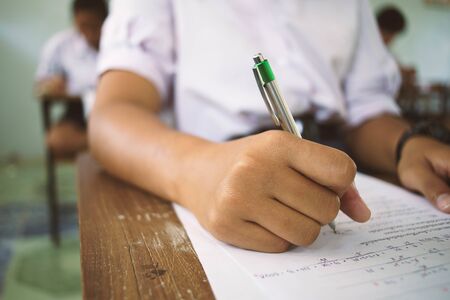 Students holding pen in hand doing exams answer sheets exercises in classroom  with stress.の写真素材