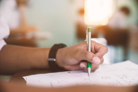 Students writing pen in hand doing exams answer sheets exercises in classroom  with stress.の写真素材