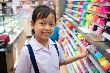 Asian uniform student girl in stationery store buying pens and school supplies. Back to school concept.の写真素材