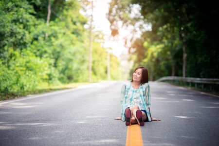 Smile asian woman sitting in the middle of the mountain road with happy and relaxの写真素材