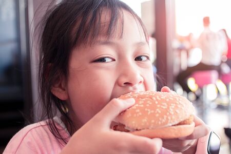 Cute asian little girl eating a hamburger in fast food restaurant.の写真素材