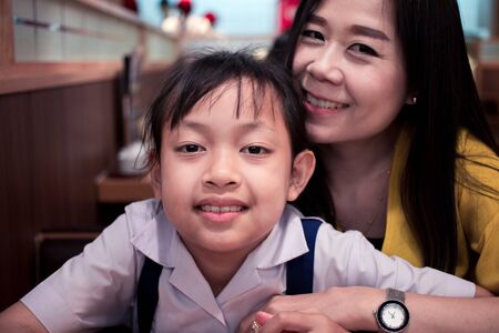 Asian daughter in uniform student and her mother smile in restaurant with happyの写真素材
