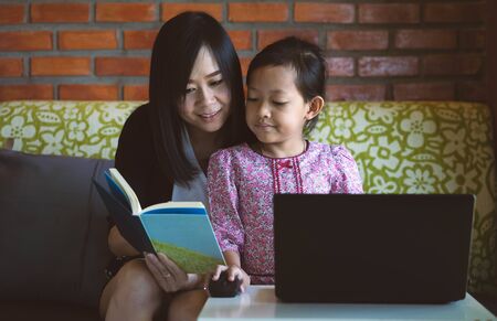 Asian daughter and mother using computer laptop at home with smile and happy.