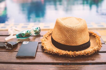The hat is placed at the wooden table side the swimming pool with smartphone and goggle.Vintage styleの写真素材