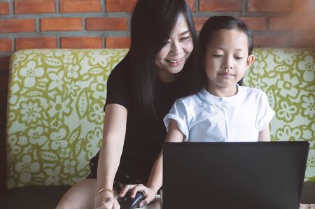 Asian Little girl playing laptop with her mother at home.の写真素材