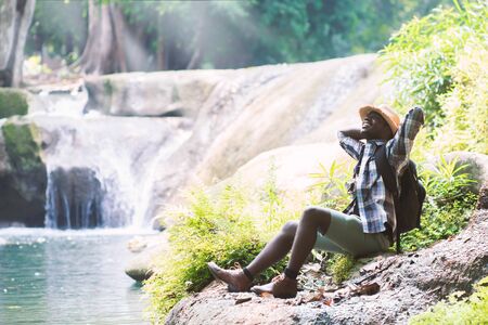 African Man Traveler with backpack sitting and relaxing freedom at waterfallの写真素材