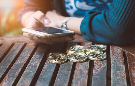 woman 's hand holding gold coin of bitcoin and use smartphone.の写真素材