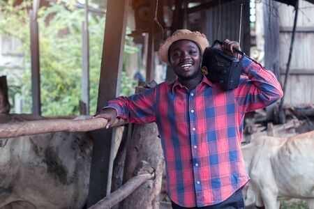 African farmer man with retro radio broadcast receiver on shoulder stands happy smiling outdoor on old cow stall backgroundの写真素材