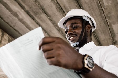 African construction engineer looking at blueprints while wearing helmetの写真素材