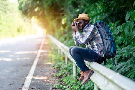 African man traveler carrying backpack and holding camera  side the highway roadの写真素材