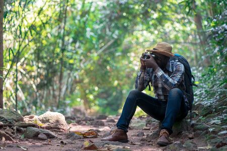 African freedom man traveler holding camera with backpack standing in the green natural forest.の写真素材
