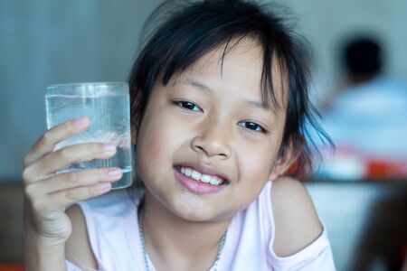 Smile asian child girl hold a glass of ice waterの写真素材