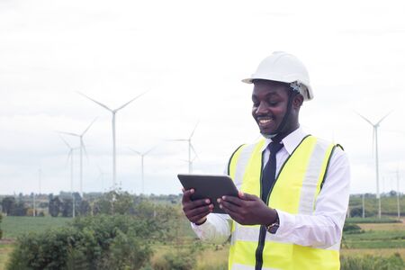 African Engineer standing and hoding laptop with wind turbineの写真素材