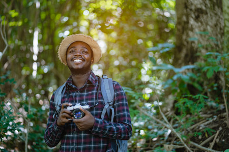 African freedom man traveler holding camera with backpack standing in the green natural forest.のeditorial素材