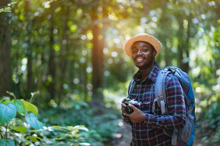 African freedom man traveler holding camera with backpack standing in the green natural forest.のeditorial素材
