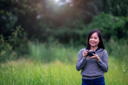 Beautiful asian woman taking picture with analog film camera in green natural background.